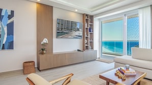 Een moderne woonkamer met een groot raam met uitzicht op de oceaan, een bank, een bijzettafeltje met boeken en een decoratieve plant.