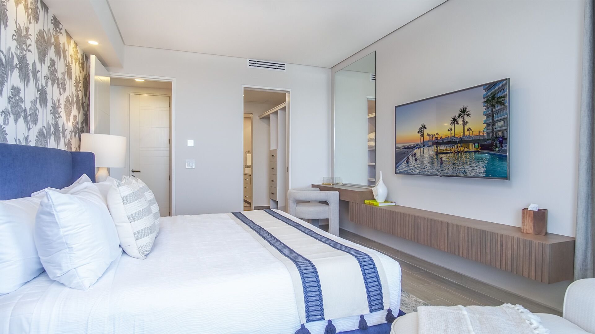 A modern hotel room with a large bed, a desk, a chair, a bathroom, and a painting of a beach scene.