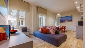 Ein modernes Wohnzimmer mit einer Couch, einem Esstisch und Stühlen. Ein großes Fenster lässt natürliches Licht herein und bietet einen Ausblick nach draußen.