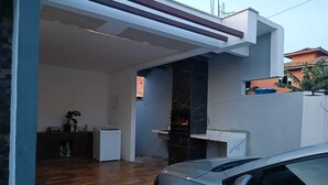Une maison moderne avec une voiture garée dans l’allée, une cheminée et un petit coin cuisine.