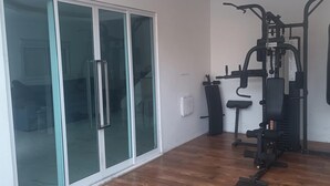 Une salle de sport équipée de matériel d’exercice, d’un sac de frappe et d’une porte-fenêtre coulissante donnant sur une pièce.