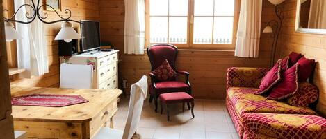 A cozy cabin interior with a wooden interior, a dining table with chairs, a sofa, and a television.