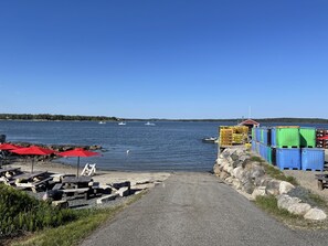 A waterfront path leading to a dock with boats, a small building, and outdoor seating with umbrellas.