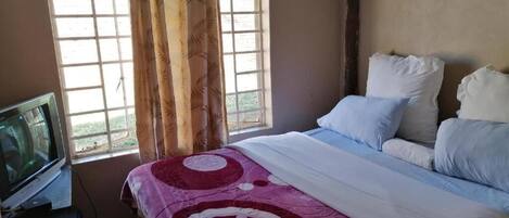 A bedroom with a bed, a television, and a window with curtains.