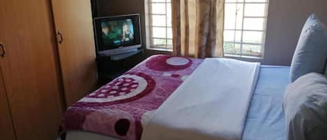 Un dormitorio con cama, televisor y ventana con cortinas.