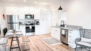 Une cuisine moderne avec des meubles blancs, des appareils en acier inoxydable et un coin repas comprenant une table et des chaises.
