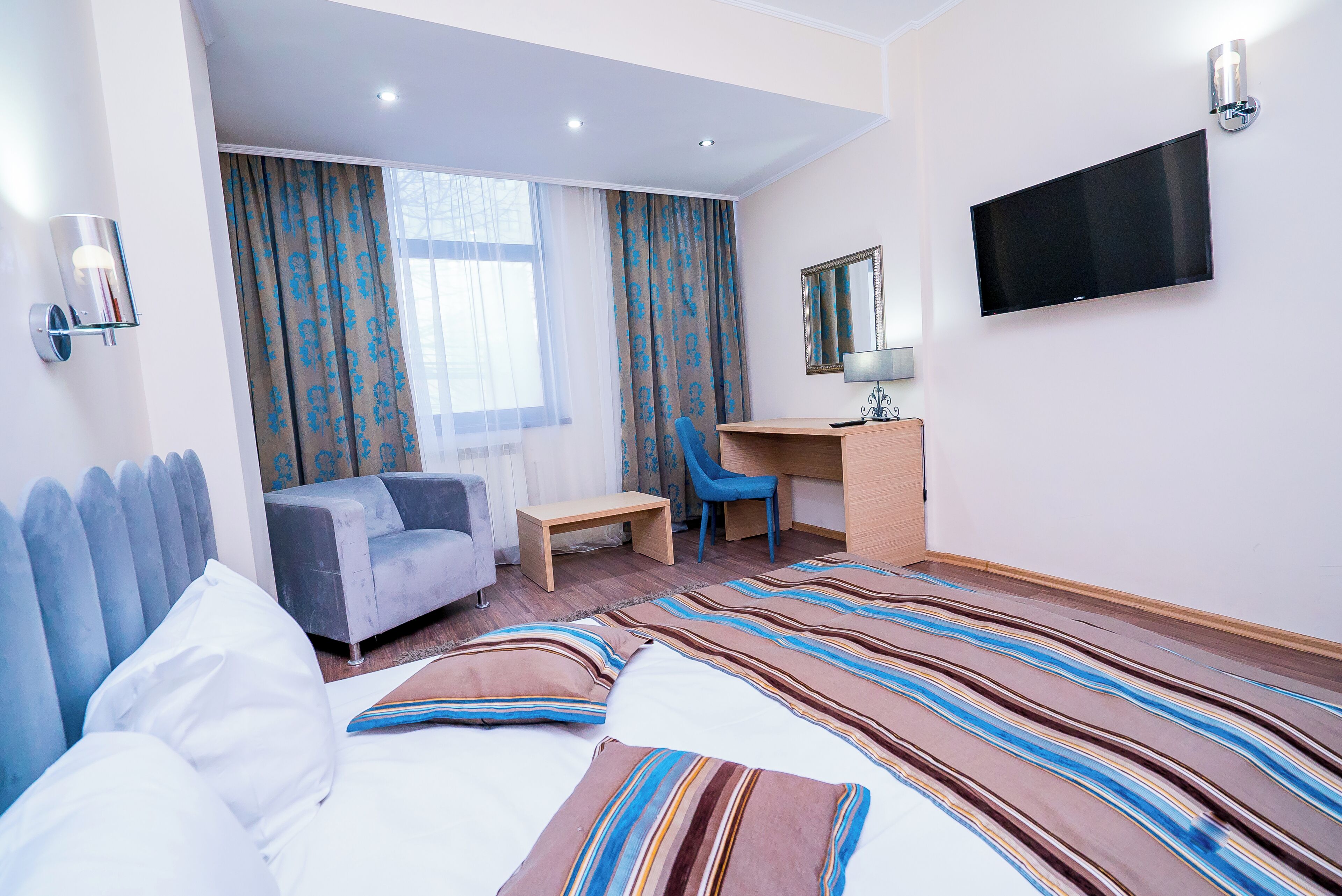 Ein Hotelzimmer mit einem Bett, einem Schreibtisch, einem Stuhl, einem Fernseher und Vorhängen.