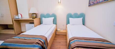 A hotel room with two beds, a desk, a lamp, a painting, and a wooden wardrobe.