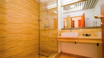 Un baño moderno con ducha envuelta en vidrio, tocador de madera y un espejo grande con marco decorativo.