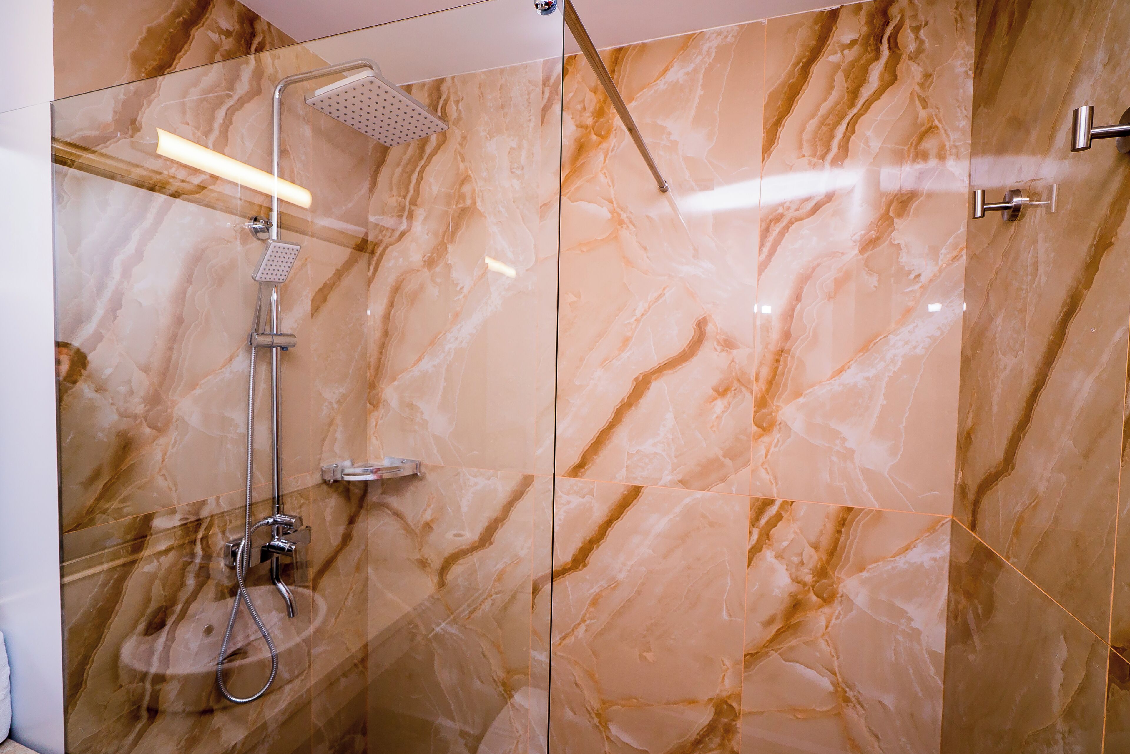 A modern bathroom with a glass shower enclosure, marble walls, and a handheld showerhead.