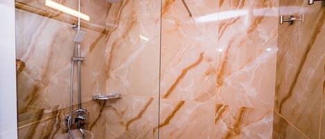 A modern bathroom with a glass shower enclosure, marble walls, and a handheld showerhead.