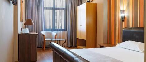 A hotel room with a bed, a desk, a chair, a small table, and a TV.