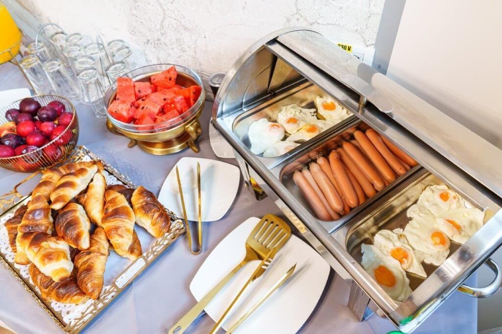 Een buffet met hotdogs, eieren, croissants, watermeloen en druiven.