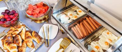 Un bufé con salchichas, huevos, cruasanes, sandía y uvas.