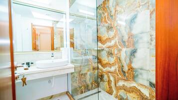 Un baño moderno con cabina de ducha de vidrio, un lavamanos blanco y paredes con diseño de mármol.
