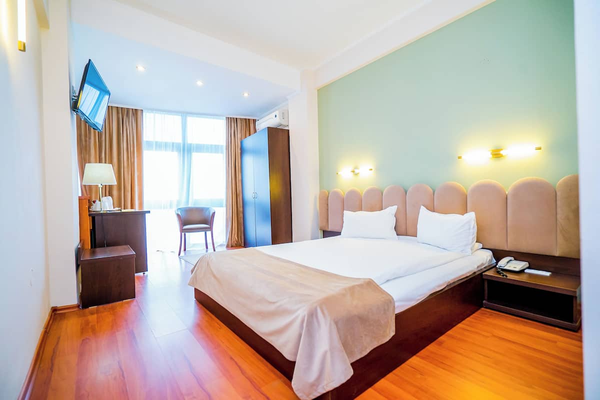 A hotel room with a large bed, a desk with a lamp, a chair, a TV mounted on the wall, and a nightstand with a phone.