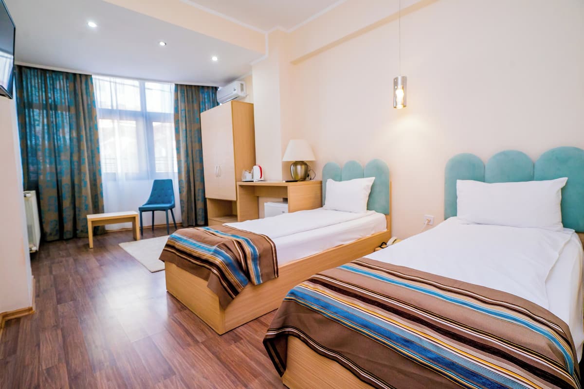 A hotel room with two beds, a desk, a chair, a TV, and a window with curtains.