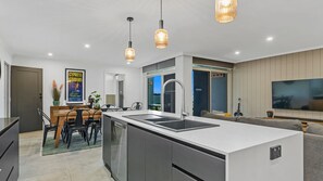 Eine moderne Küche mit einer zentralen Kochinsel, einem Essbereich mit Tisch und Stühlen, einem Einbauofen und Pendelleuchten.