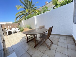 A patio with a round wooden table and two wooden chairs, surrounded by a white wall and a tiled floor.