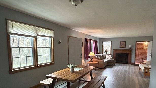 A spacious living room with a wooden dining table, benches, a sofa, and a fireplace. - Charming House surrounded by woods, close to Windrock and Lake Norris (Rocky Top)