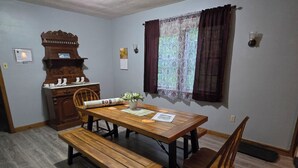 A dining area with a wooden table, benches, and chairs. There is a wooden cabinet with a mirror and a wall-mounted light fixture. - Charming House surrounded by woods, close to Windrock and Lake Norris (Rocky Top)