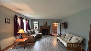 A living room with a fireplace, two sofas, a coffee table, and a lamp. - Charming House surrounded by woods, close to Windrock and Lake Norris (Rocky Top)