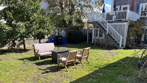 Ein Garten mit einer Holzterrasse, einer weißen Treppe und einer Terrasse mit Tisch und Stühlen.