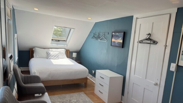 Ein Schlafzimmer mit Bett, Schreibtisch, Stuhl, Kommode, Kleiderstange und einer Tür.