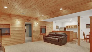 A log cabin interior with a leather sofa, wooden walls, a kitchen area, and a dining table. - Shamrock- Aunt Susie's- Raystown Lake- 7 Points (Hesston)