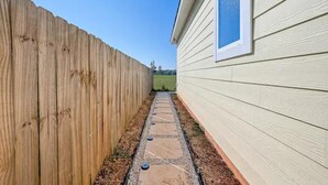 A narrow pathway with a wooden fence on one side and a building on the other. - Cozy Home Lake Conroe

 (Montgomery)