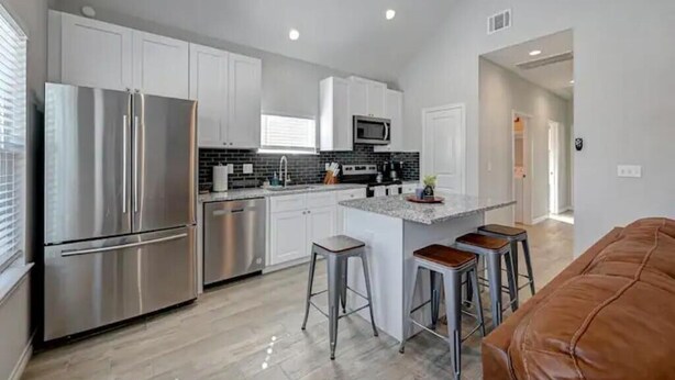 A modern kitchen with stainless steel appliances, white cabinets, and a central island with stools. - Cozy Home Lake Conroe

 (Montgomery)