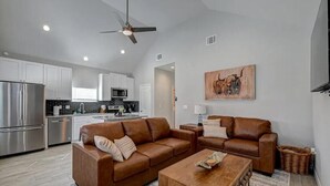 A modern kitchen with stainless steel appliances, a dining area with a brown leather sofa, and a painting on the wall. - Cozy Home Lake Conroe

 (Montgomery)