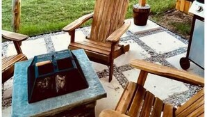A patio with wooden chairs and a table, a grill, and a view of a green field. - Cozy Home Lake Conroe

 (Montgomery)