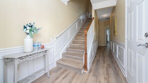 A hallway with a wooden staircase, a white console table with decorative items, and a door on the right.