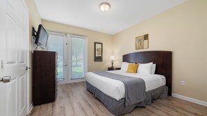 A bedroom with a bed, a TV mounted on the wall, a door, and a window with blinds.