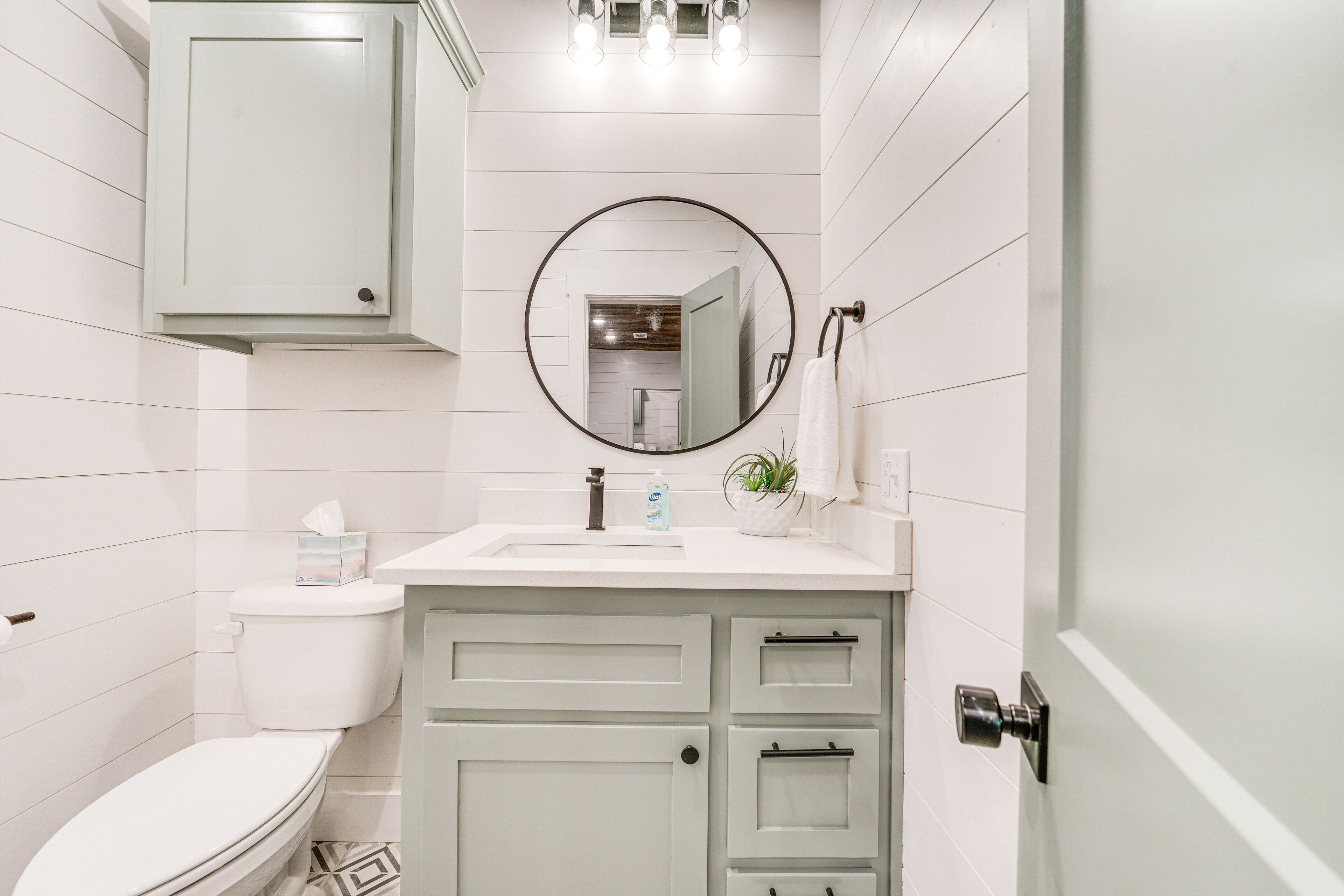 A bathroom with a toilet, sink, mirror, and cabinets.