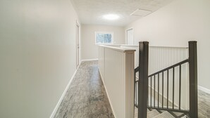 Un couloir doté d’un plancher en bois, de murs blancs et d’une rambarde noire menant à un escalier.