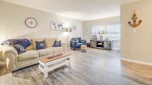 Un salon avec un canapé beige, une table basse en bois et un fauteuil bleu. Un planisphère est accroché au mur, et une décoration représentant un gouvernail de navire est également présente.