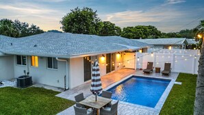 Ein Garten mit Swimmingpool, überdachter Terrasse und Essplatz.