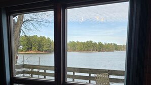 Un espace repas avec une table et des chaises, une vue sur un lac et une terrasse en bois à l’extérieur.
