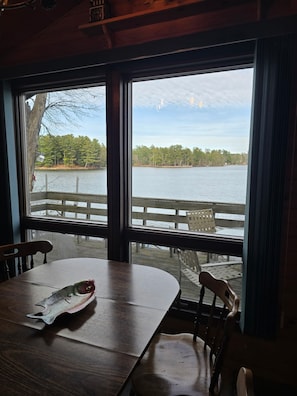 A dining area with a table and chairs, a view of a lake, and a wooden deck outside. - Cozy 2 Bedroom LAKE FRONT Cabin on Chetek Chain of Lakes, GREAT LOT & LOCATION! (Chetek)