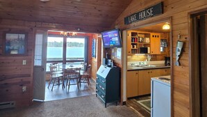 L’intérieur d’une cabane comprenant un coin repas, une cuisine et une pancarte sur laquelle on peut lire : « MAISON AU BORD DU LAC ».