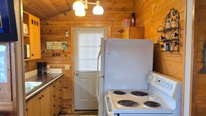 Une cuisine aux murs en bois, avec un poêle, un évier et une pancarte de bienvenue.