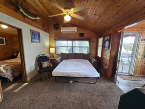 A log cabin room with a bed, a chair, a ceiling fan, and a window.