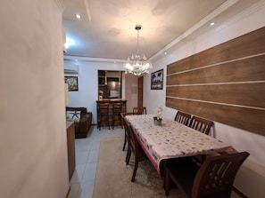 A dining area with a table set for four, a chandelier, and a kitchen in the background.