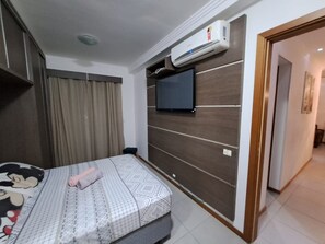 A bedroom with a bed, a TV mounted on the wall, and an air conditioning unit above the bed.