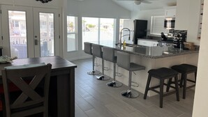 A modern kitchen with a bar area, large windows, and a ceiling fan.