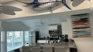 A modern kitchen with a central island, bar stools, a ceiling fan, and a large fish mural on the wall.
