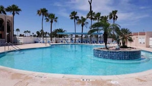 A swimming pool with palm trees, lounge chairs, and a clear blue sky.