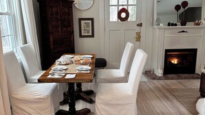 Un comedor con una mesa de madera, sillas blancas, un reloj y una chimenea.